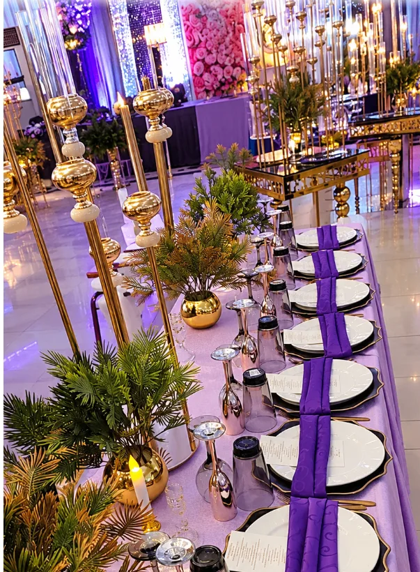 Elegant banquet table with gold candelabra, green foliage, white plates, and deep purple napkins