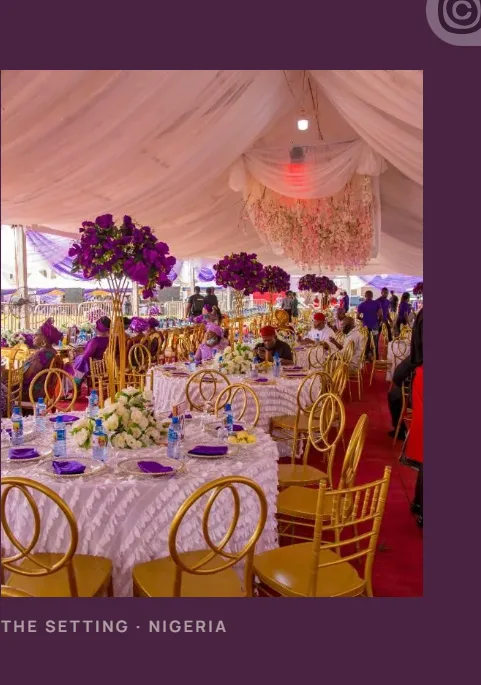 Draped tent with round tables, purple and white florals, red carpet, and gold chairs
